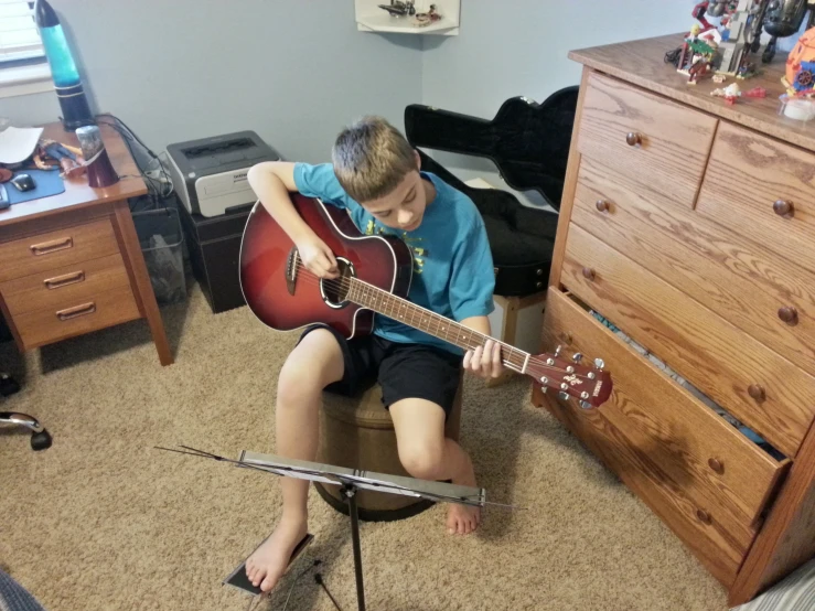 a boy sits in the corner and holds a guitar in his hands