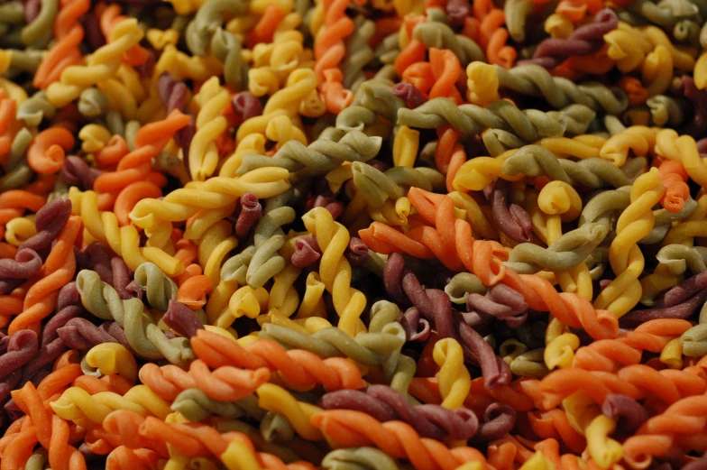 many colorful pastas are being tossed up into a pile