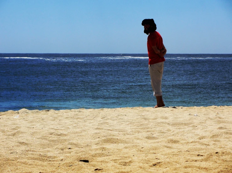 man standing on sandy beach facing ocean with boat