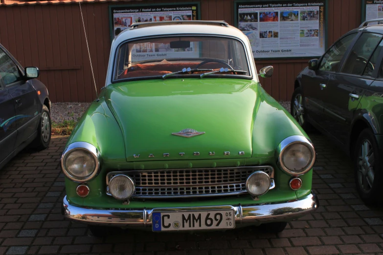 an old green car sits in a brick parking lot