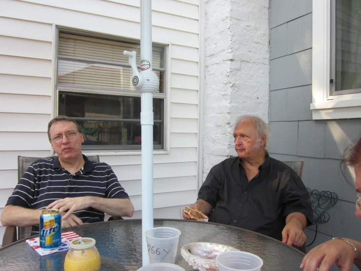 three people sitting at a table outside of a home