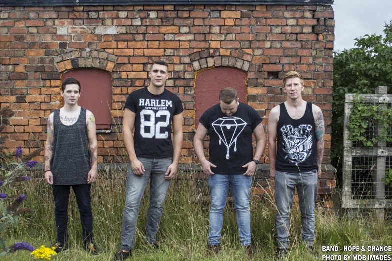 six young men stand next to a brick building