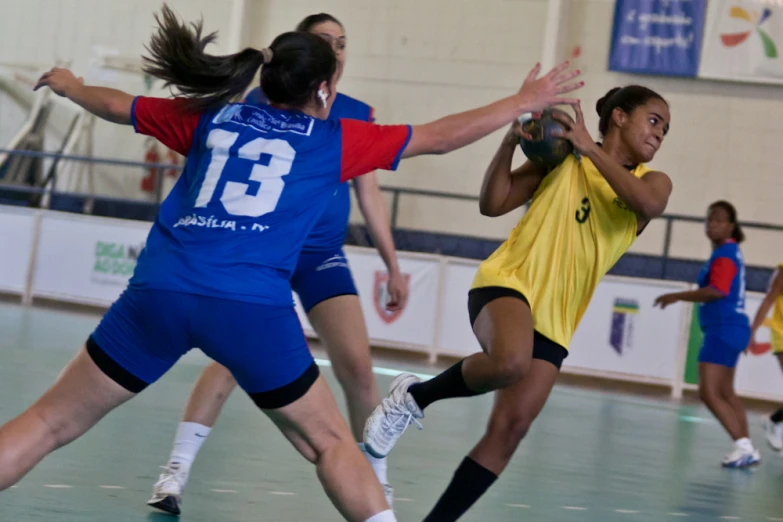 two women playing soccer on a field while one in yellow watches the ball