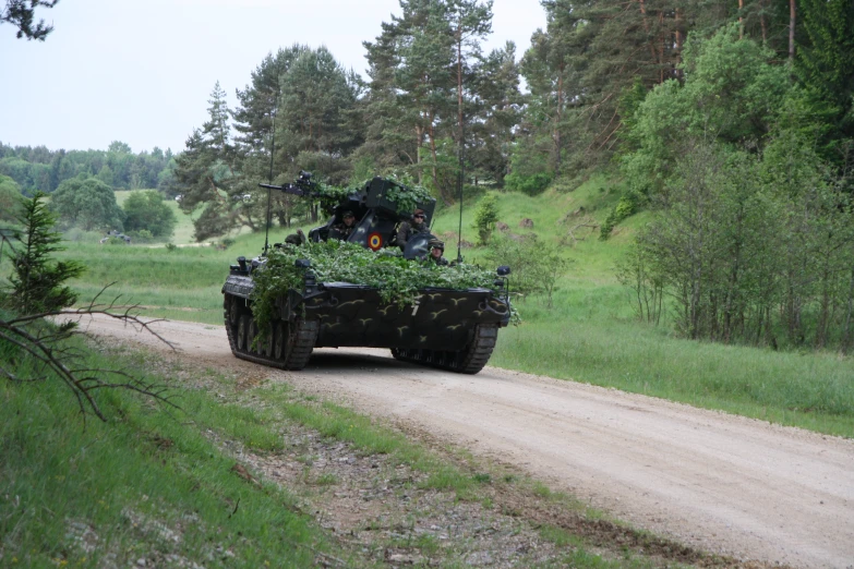 an army tank driving down a dirt road next to a forest