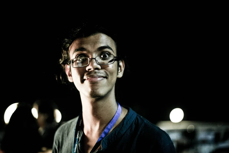 a man wearing glasses with a smile in the dark