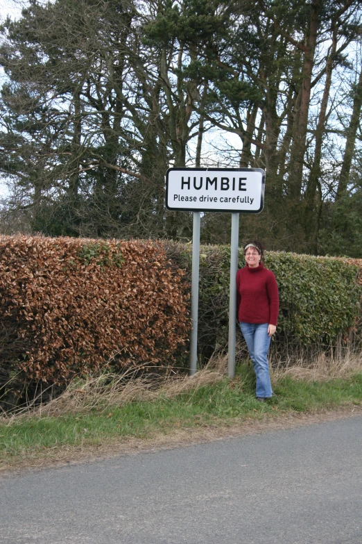 woman standing underneath humbie crossing sign next to road