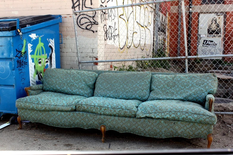 a couch and a trash can in front of a fence