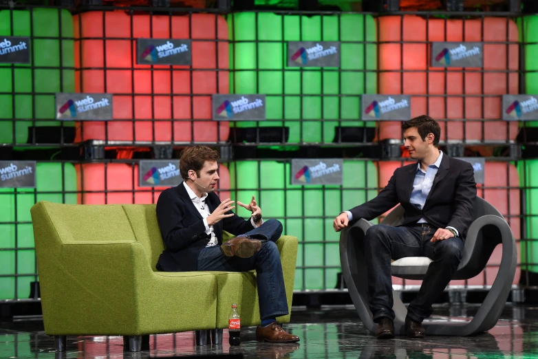 two men sitting on chairs in front of stacks of television boxes