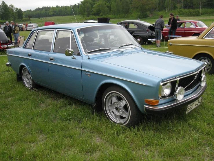 two classic cars sitting in the grass near others