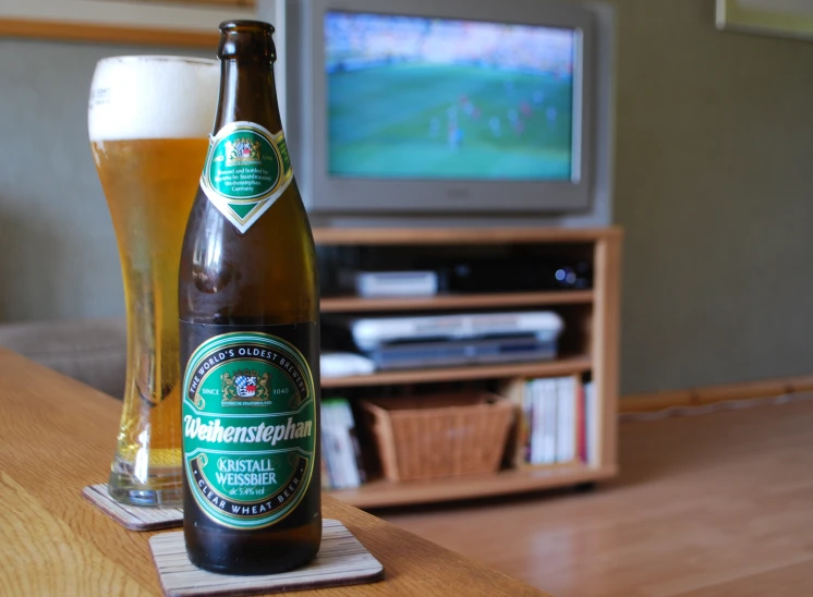 two beer bottles are on a table with a television in the background