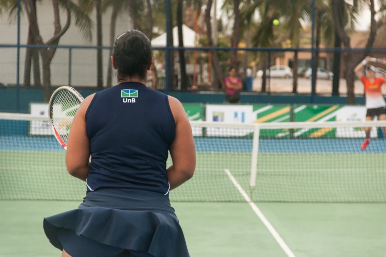 the back view of a woman standing in front of a tennis net
