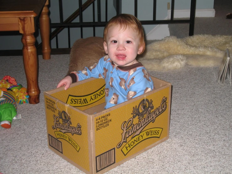 a baby boy inside a cardboard box while sitting on the ground