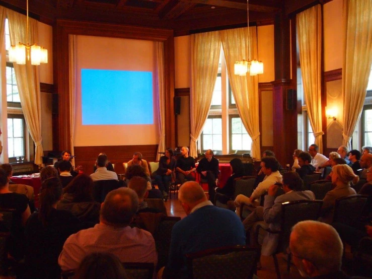 people are seated in the large hall listening to one man talk