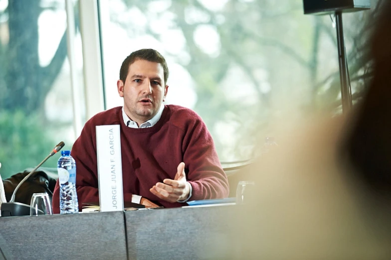 a man with a red sweater sits at a table and speaks