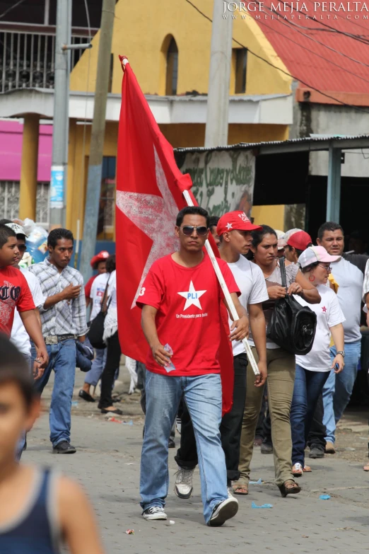 a crowd walking in street with a flag in the background