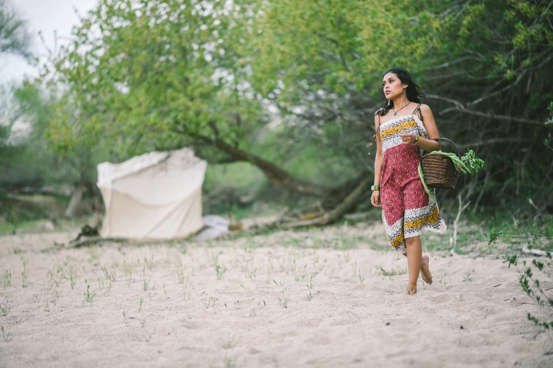 a woman is carrying soing in her hand and standing in the sand