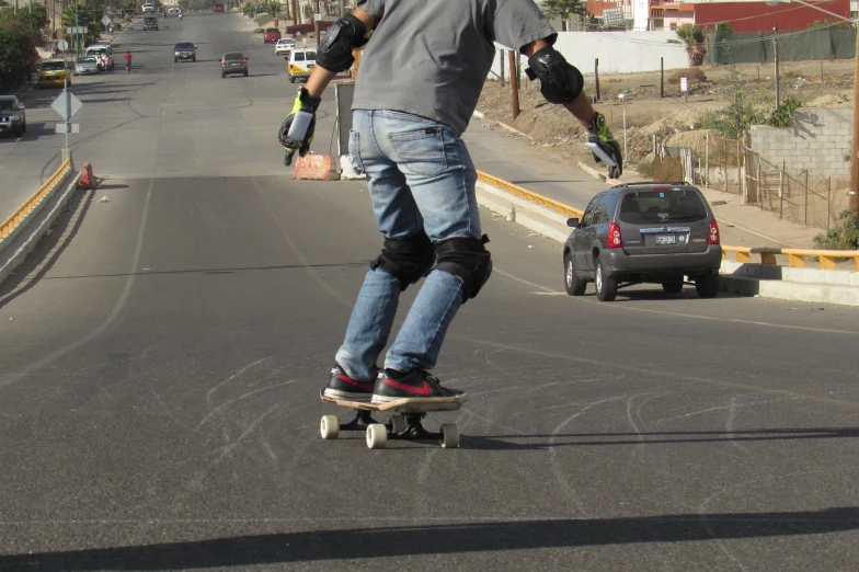 a young man wearing pads and riding a skateboard down a city street