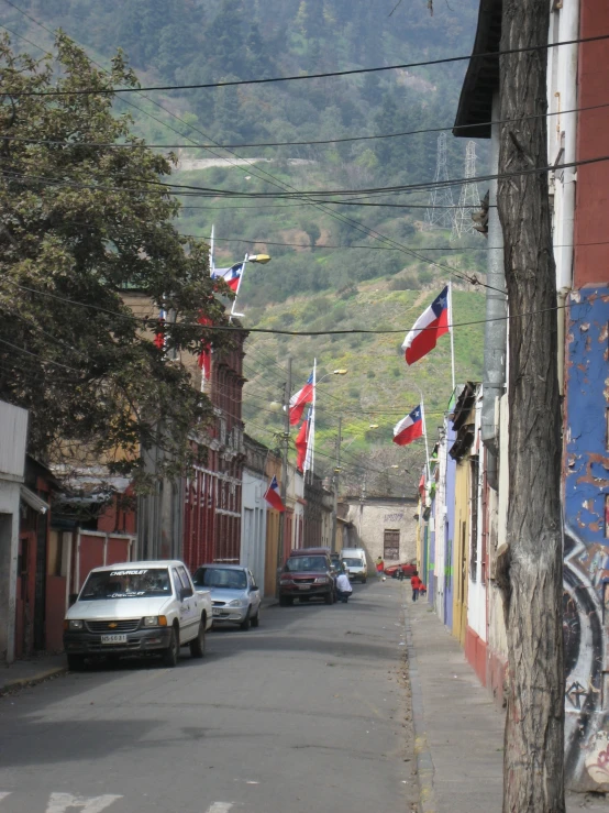 a city street lined with parked cars and covered in flags