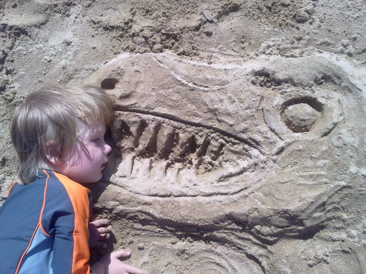 the boy is playing with the sand near a fossil