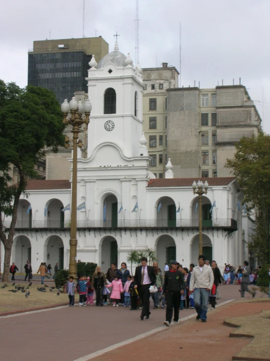 people walk down a street in front of a white church