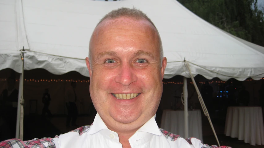 man smiling at camera with white tent behind him