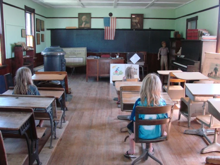 several children are sitting at desks in an empty room