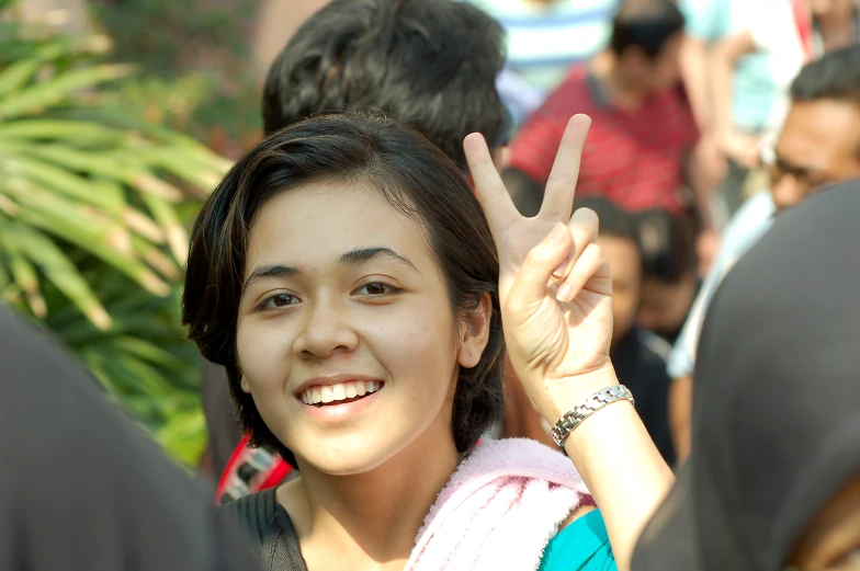 the young woman smiles as she gives a peace sign