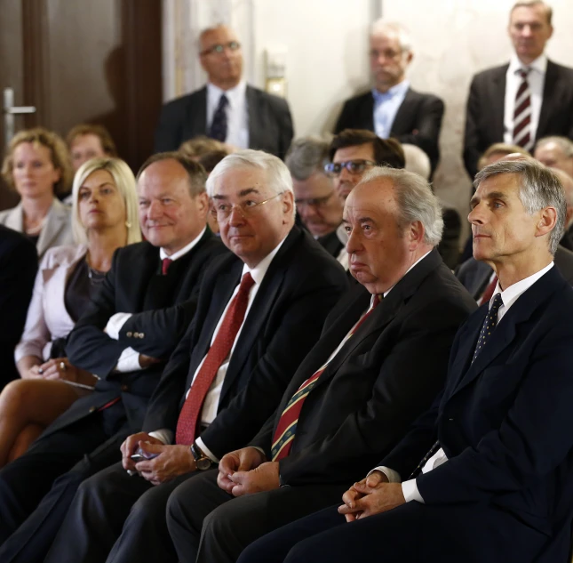 several men sitting and one is wearing a suit and tie