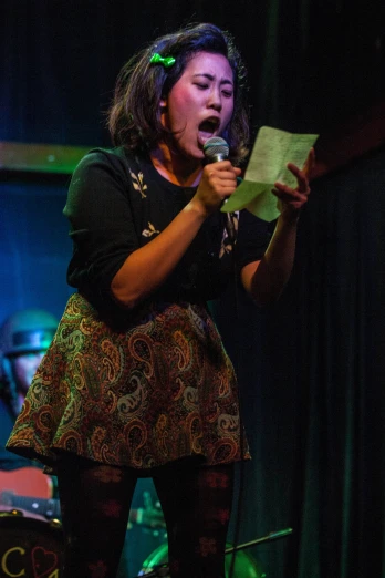 a woman sings into a microphone while holding a sheet of paper