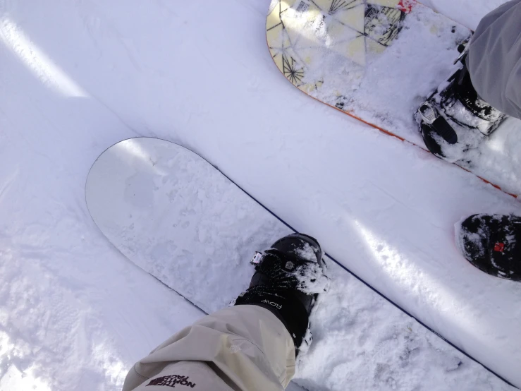 two people standing in the snow with their feet up