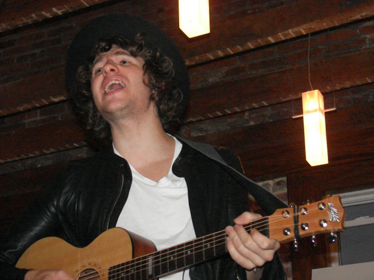 a man with long hair wearing a hat and playing an acoustic guitar