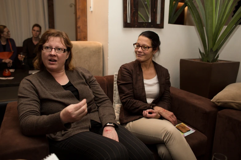 two women sitting on top of a brown couch