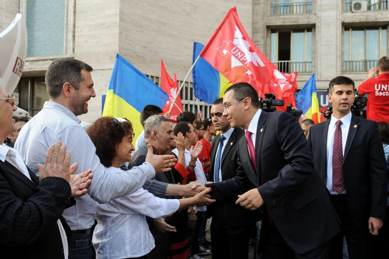 a man in a suit and tie shaking hands with people holding red, yellow and blue flags