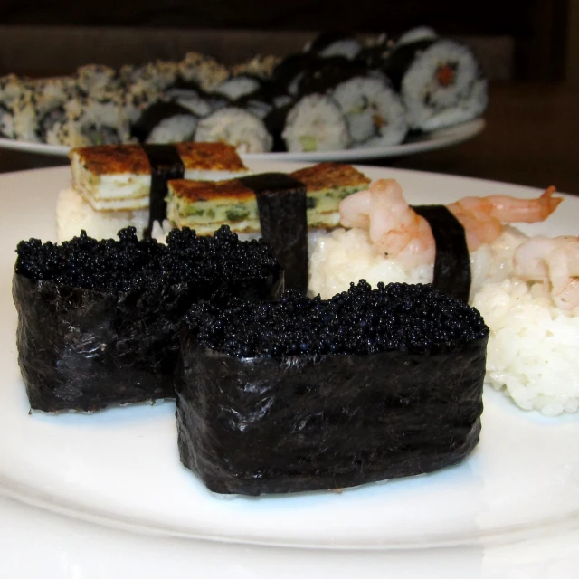 several kinds of sushi on white plates on a table