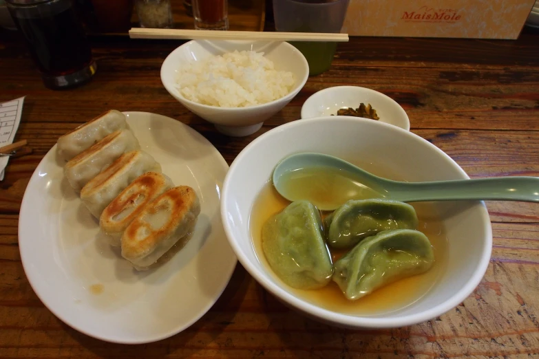 a bowl of soup is sitting on a table next to a plate with three pieces of  dogs