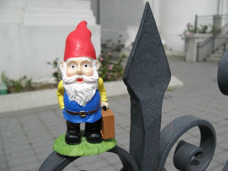 a gnome with luggage is holding soing near a fence