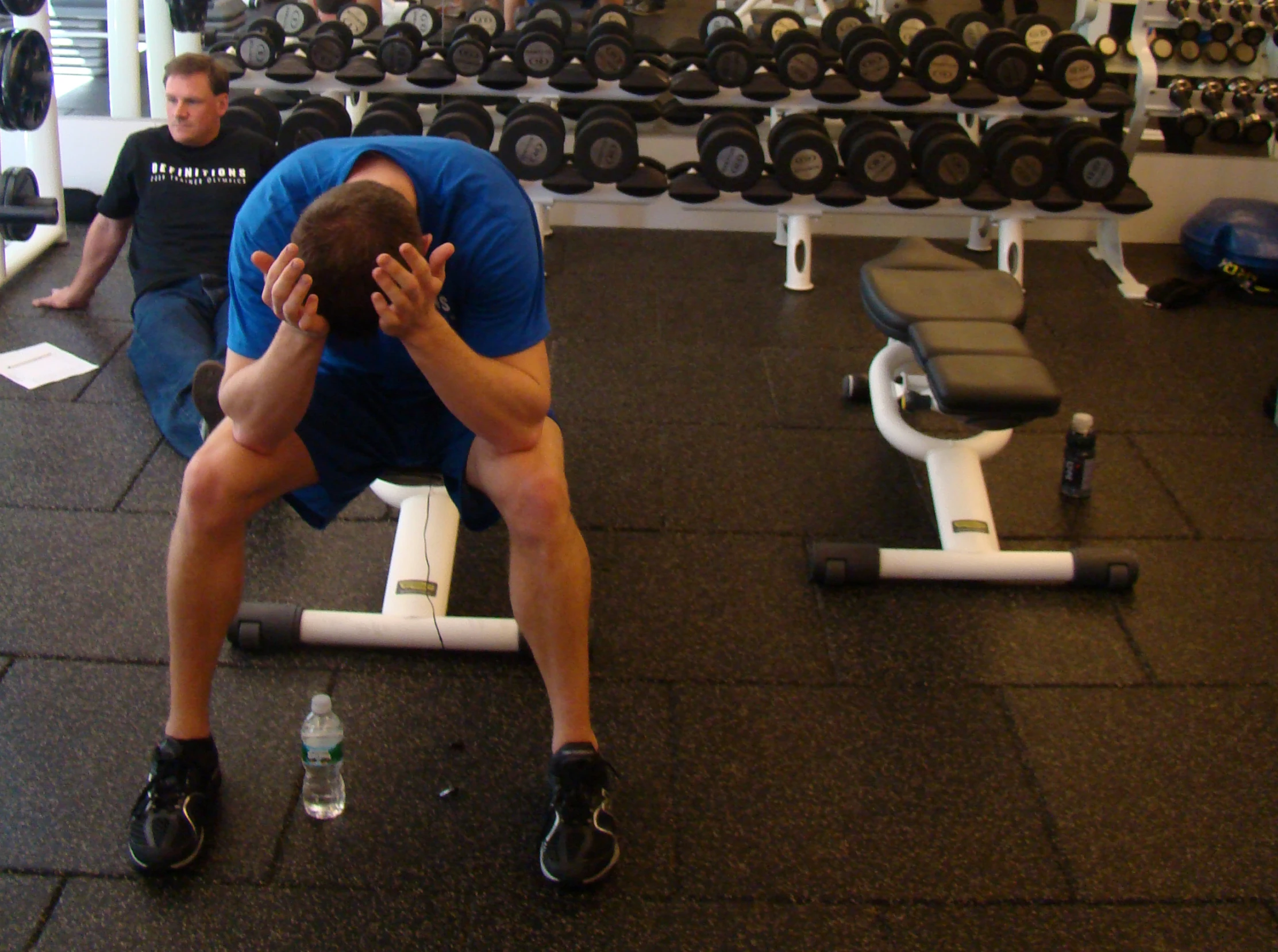 a man sitting in the middle of the gym bench with a man looking down as if to exercise