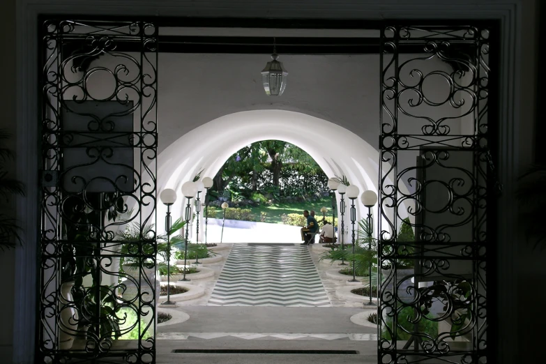 a large white archway leads to a well maintained garden