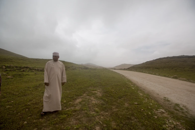 a man standing in a grassy field on a cloudy day