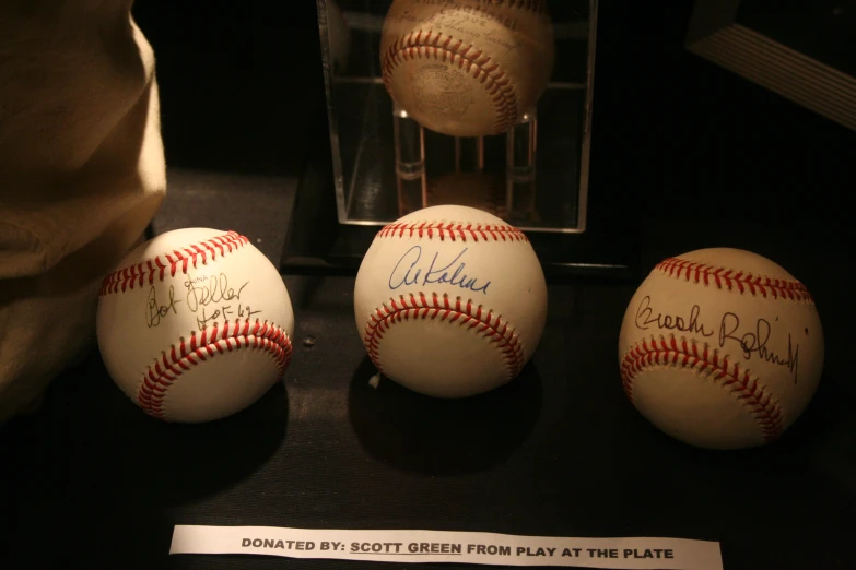 three baseballs with signed caps sitting inside of a case