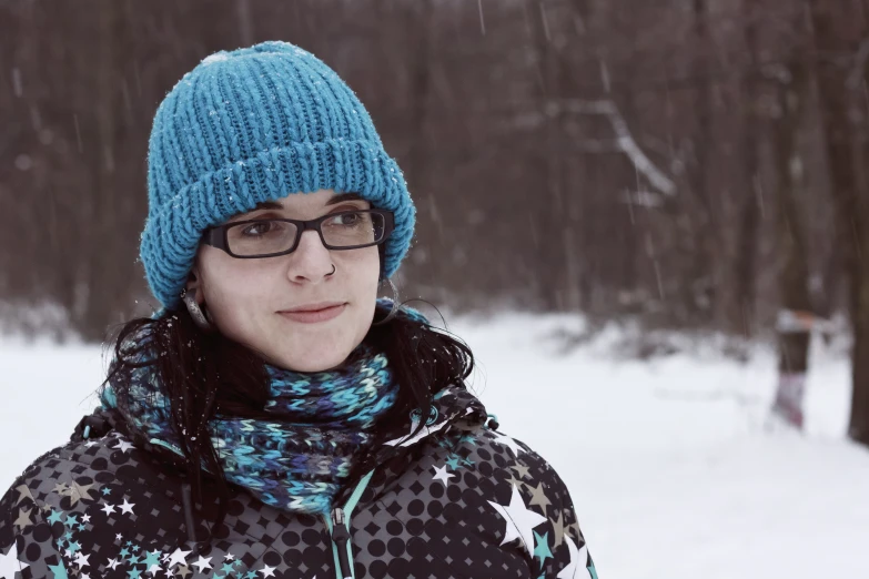 a woman wearing a knitted hat and sweater in front of snow covered trees