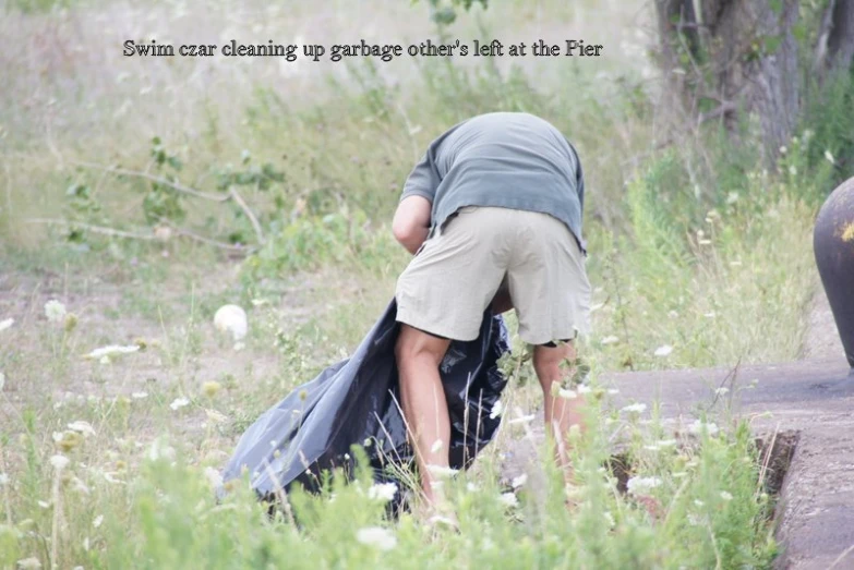 man crouched over outside holding onto trash in weeds