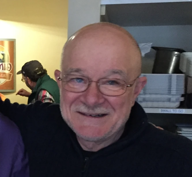 a bald man in black shirt smiling in a kitchen