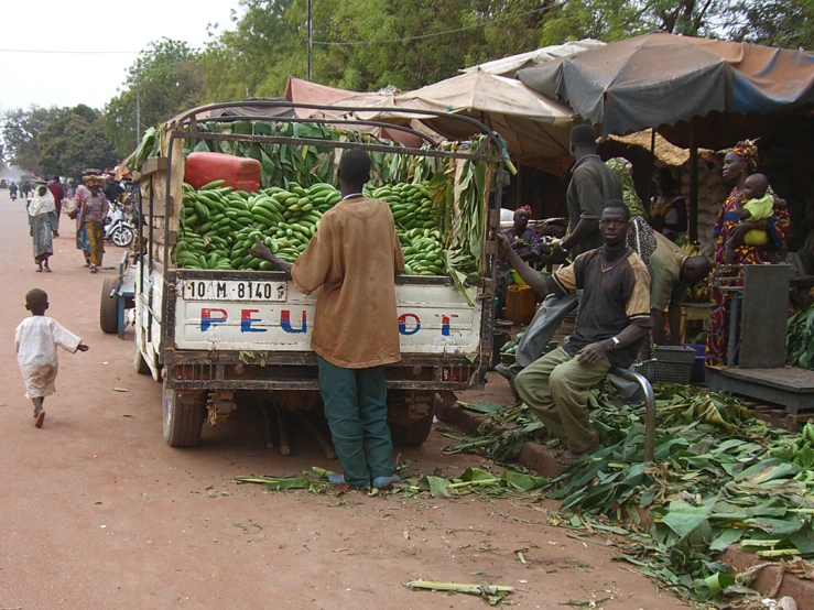 a street scene with a man in the back and two children walking towards produce on display