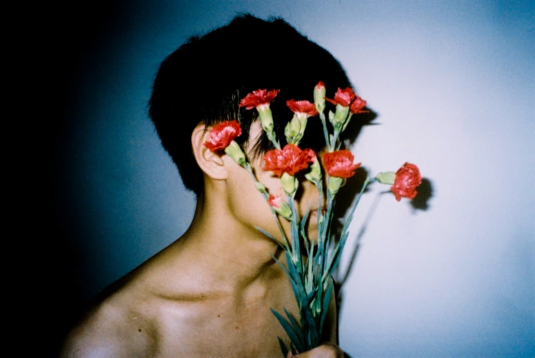 a boy holding red flowers over his face