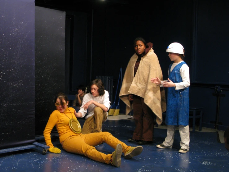 people wearing orange and white sit in front of a stage with blue walls