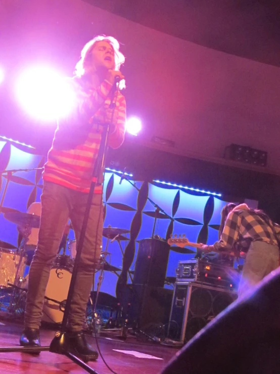 a man on stage singing into microphone while an adult plays the guitar behind him