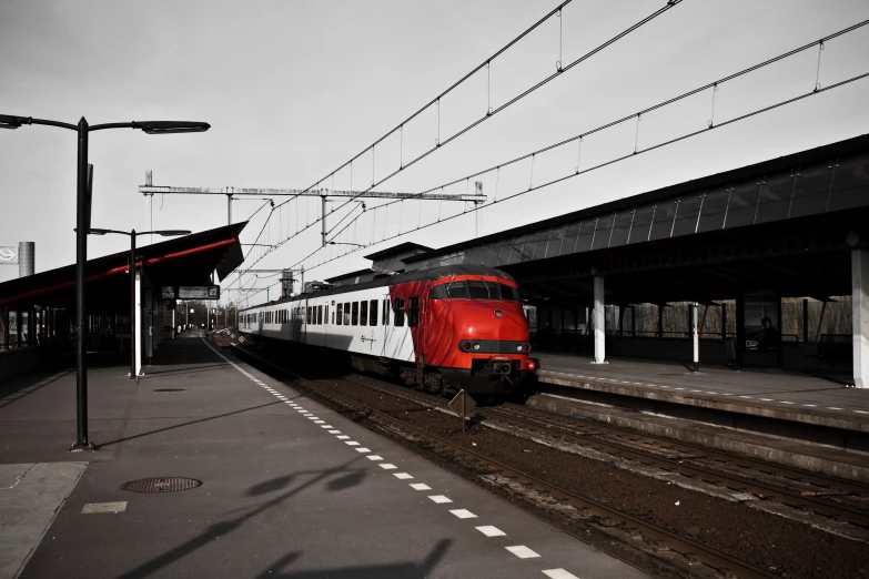 a red and white train at a platform with power lines above it