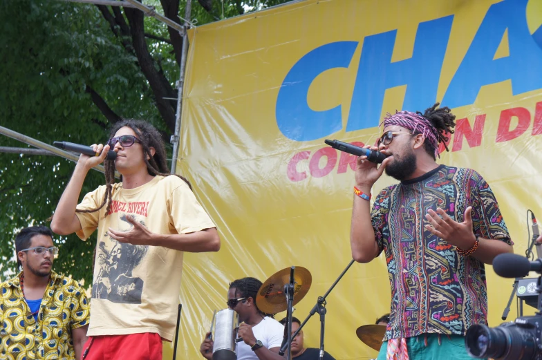 a man singing into a microphone on stage with other men in the background