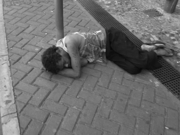 a man laying on the sidewalk next to a pole